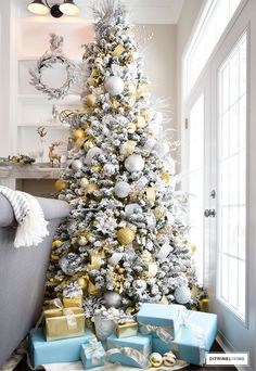 a white christmas tree with gold and silver ornaments, presents under the tree in front of it