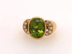 This vintage Italian-made peridot ring is a remarkable piece, reflecting timeless elegance and fine craftsmanship. Fashioned from solid and heavy 18k yellow gold, the ring showcases a classic bezel setting that securely encases the oval peridot.  Five round brilliant cut diamonds on each side of the oval peridot, making a total of ten diamonds. The ring's design is accentuated by a carefully crafted gallery beneath the stones, allowing light to flow through and enhance the natural brilliance of the peridot and diamonds. The substantial weight and sturdy construction speak to its durability, while the vintage charm adds a unique character to this luxurious piece. Specs:  Stamped 18k and M Genuine peridot and diamonds  Size 6 1/2 finger size Peridot Ring, Precious Gemstones, Diamond Sizes, Round Brilliant Cut Diamond, Semi Precious Gemstones, Vintage Charms, Rings Statement, Ring Designs, Semi Precious