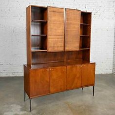 a large wooden cabinet with two doors and shelves on one side, against a white brick wall