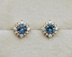 two pairs of blue and white diamond stud earrings on a white surface with the top one in