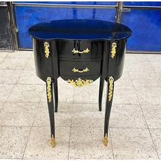 a black and gold painted table with two drawers on each side, in front of a blue wall