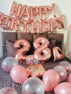 a bed topped with lots of pink and silver balloons next to a sign that says happy birthday