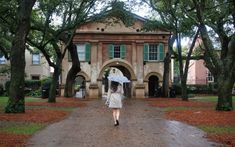 a woman with an umbrella walks down a path in front of a large brick building