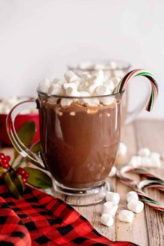 hot chocolate with marshmallows and candy cane in a glass mug on a wooden table