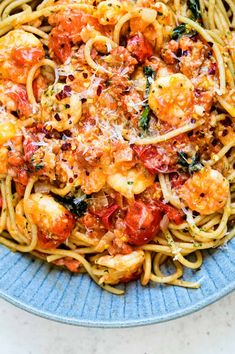 pasta with shrimp, tomatoes and parmesan cheese in a blue bowl on a white table