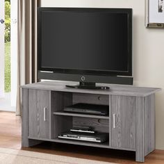 a flat screen tv sitting on top of a wooden entertainment center next to a window