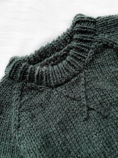 a close up of a green sweater on a white surface with the top stitched off