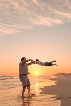 a father and son playing on the beach at sunset with their arms in the air