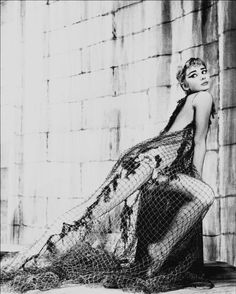 a woman in a fish net dress leaning against a wall