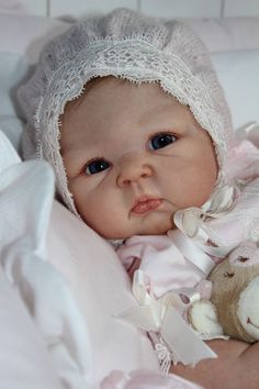 a baby in a white bonnet holding a teddy bear