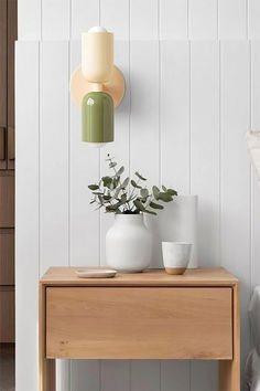 a wooden table topped with white vases next to a wall mounted light above it