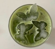 a glass filled with green liquid on top of a white table next to an orange slice