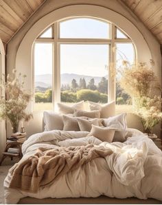 a large bed sitting under a window next to a wooden floor covered in blankets and pillows