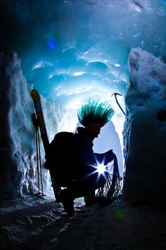 a man with green hair sitting in front of an ice cave while holding skis