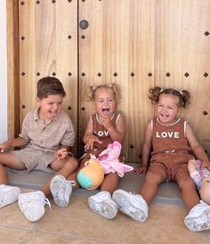 three young children sitting on the floor laughing and playing with stuffed animals in front of wooden doors