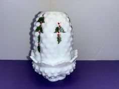 a white vase with holly on it sitting on a purple tablecloth next to a wall