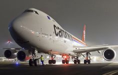 an airplane is sitting on the tarmac at night with its lights on and people standing around it