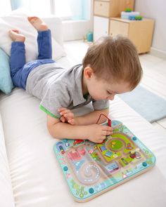 a little boy laying on top of a bed playing with a toy laptop and pen