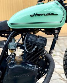 the front end of a green motorcycle parked next to a brick sidewalk and building with a sign that reads honda on it