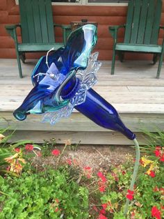 a blue glass sculpture sitting on top of a wooden deck next to flowers and chairs