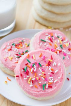 three pink frosted donuts with sprinkles on a plate next to a glass of milk