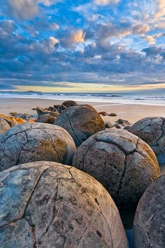 some large rocks sitting on top of a sandy beach under a blue sky with clouds