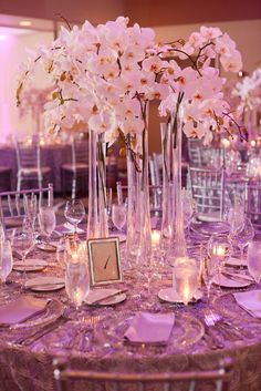 the table is set up with purple linens and white flowers in tall vases