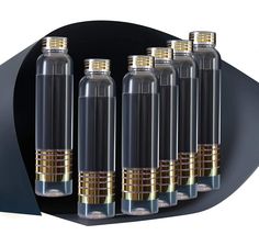 six glass bottles with gold rims are lined up on a black surface, in front of a white background