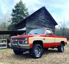 a red and tan truck parked in front of a barn