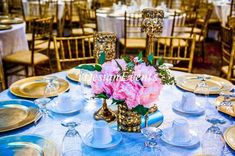 a blue table cloth topped with plates and vases filled with pink flowers on top of it