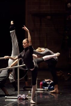 three ballet dancers in black and white outfits, one holding the bars with her arms