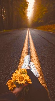 someone's feet resting on the side of an empty road with a sunflower