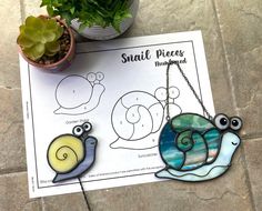 two snails on a sheet of paper next to a potted plant