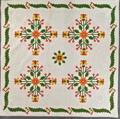 a white quilt with orange and yellow flowers on the front, green trim around the edges