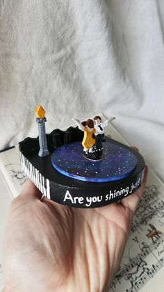 a hand holding a small toy with two people on it and the words are you shining?