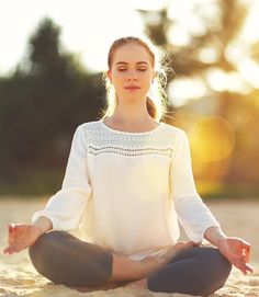 a woman is sitting in the sand and meditating