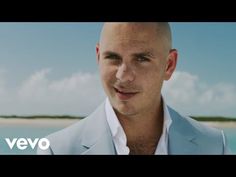 a bald man wearing a blue suit and white shirt standing in front of the ocean