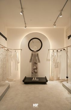 a room filled with lots of white dresses and mannequins in front of a circular window