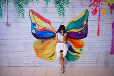 a woman standing in front of a wall with a painted butterfly on it's wings