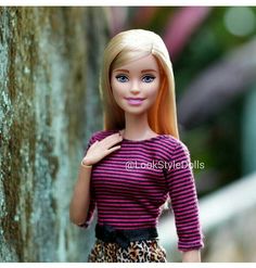 a barbie doll standing next to a tree wearing a purple and black striped shirt with leopard print skirt