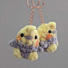 two stuffed animals are hanging from chains on a keychain, one is yellow and the other is gray