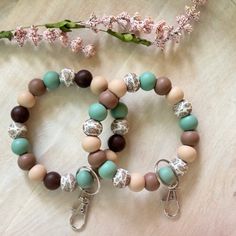 two bracelets with charms on them sitting next to a pink flower and some flowers