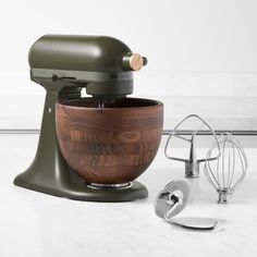 an olive green stand mixer with wooden bowl next to other kitchen accessories and utensils