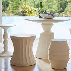 three white vases sitting next to each other on top of a table in front of a pool