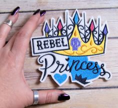 a woman's hand with black nail polish holding up a princess patch