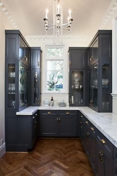 a large kitchen with black cabinets and white counter tops, wood flooring and chandelier