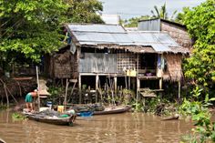 two people standing on a boat in front of a shack with corrugated roof and metal roofs