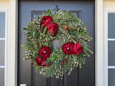 a wreath with red flowers and greenery is hanging on the front door of a house