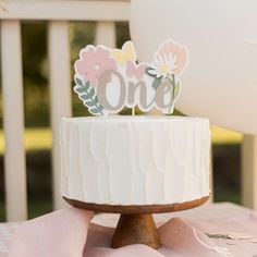 a white cake sitting on top of a wooden table next to a pink and yellow blanket