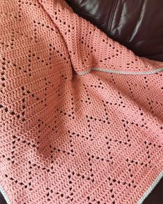 a pink crocheted blanket sitting on top of a leather couch